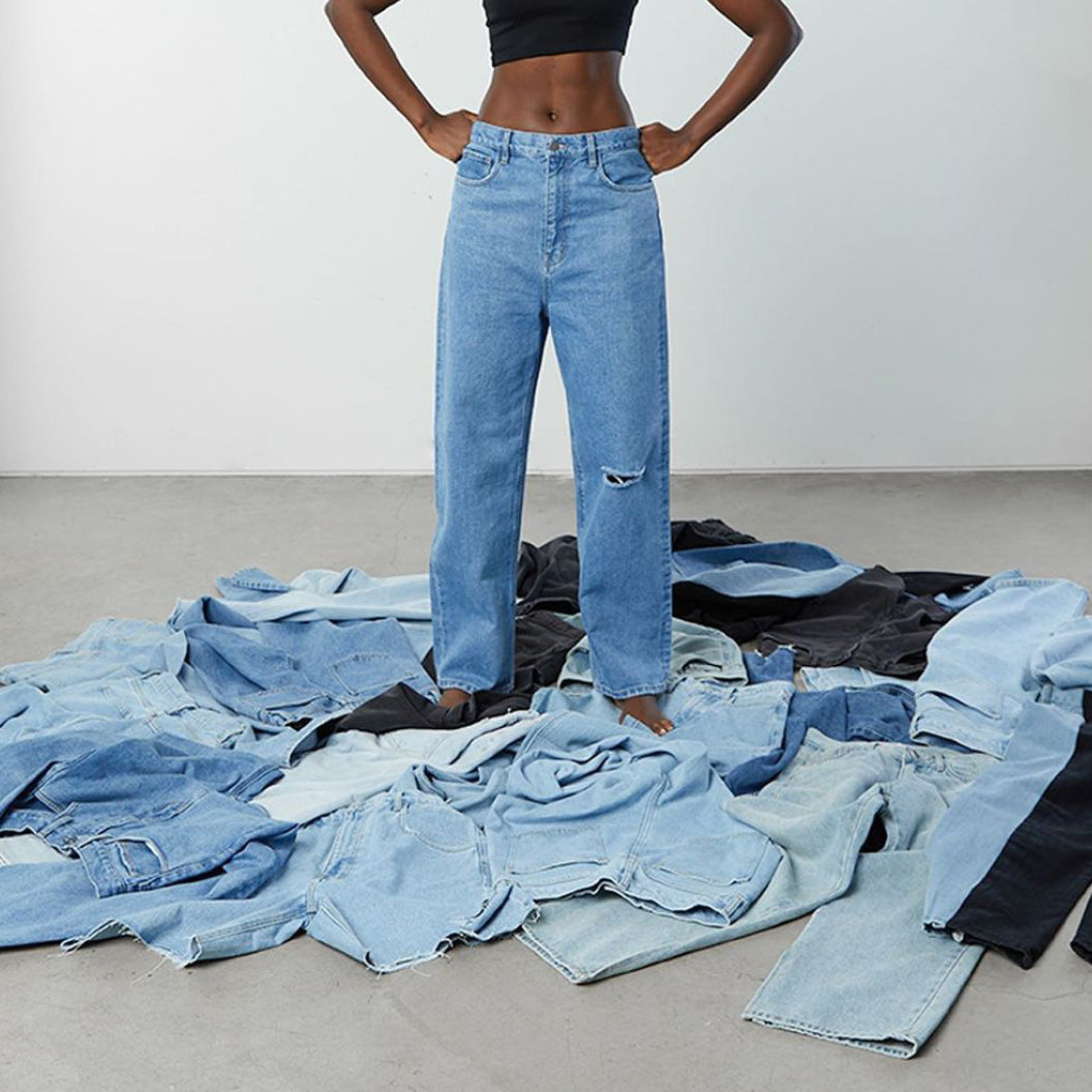 Model in black OAK + FORT top and OAK + FORT jeans standing on a pile of OAK + FORT jeans 
