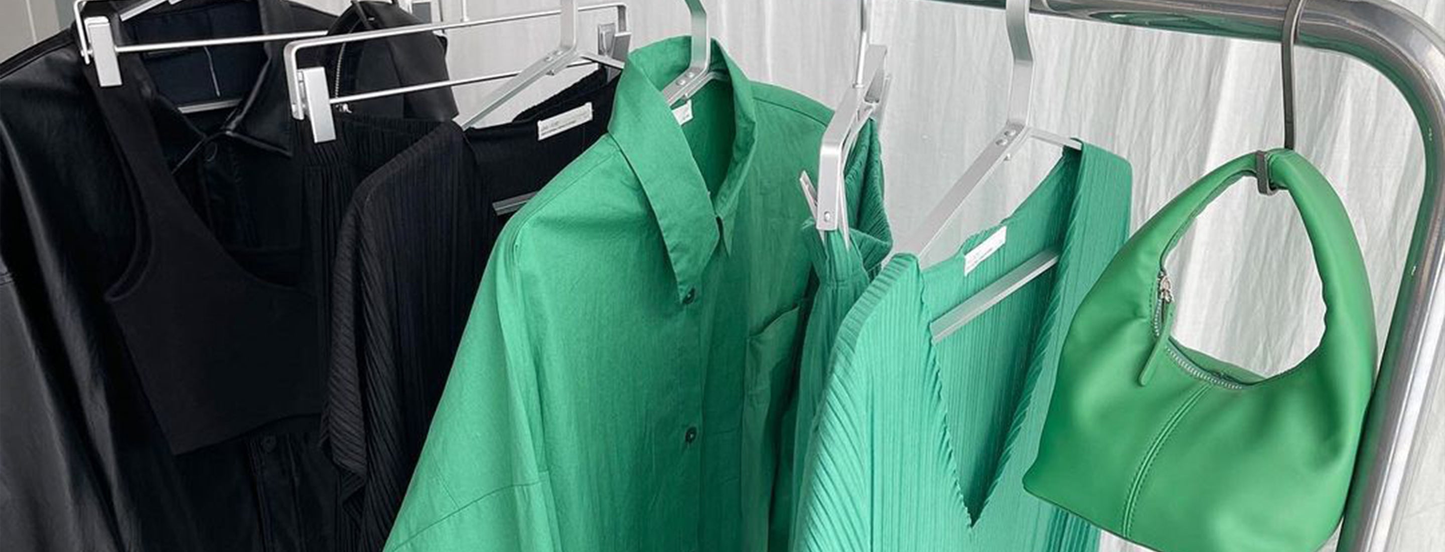 Black and green OAK + FORT clothing and a green OAK + FORT handbag hanging on a rack 